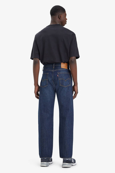 Jean droit en denim bleu moyen de Levi's®, avec une étiquette de marque en cuir visible et porté avec un t-shirt noir.