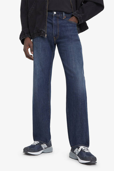 Jeans droit bleu moyen de Levi's®, portés avec une veste noire et des baskets bleu marine.