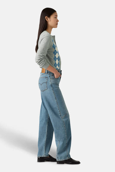 Jeans ample en denim bleu clair de Levi's, avec des poches et portés avec un cardigan gris à losanges.
