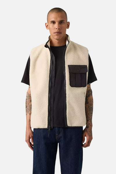 Veste sans manches beige de Levi's®, avec une poche plaquée noire et fermeture éclair, portée sur un t-shirt noir et un jean bleu foncé.