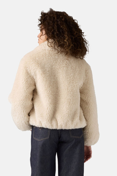 Korte beige jas van Levi's® met schapenvachttextuur en zakdetails op een donkere broek.
