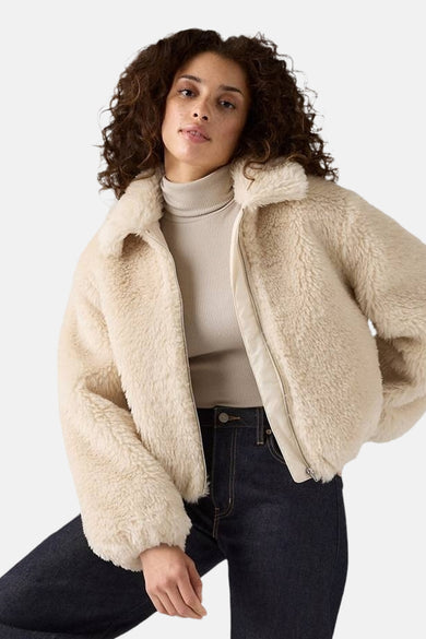 Korte beige jas van imitatie schapenvacht van Levi's®, gedragen met een coltrui en een donkere jeans.