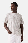 T-shirt à manches courtes beige de Levi's® avec motif imprimé sur fond blanc, porté avec un pantalon blanc.
