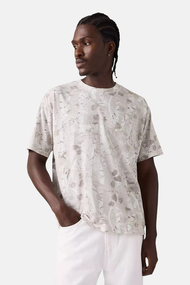 T-shirt à manches courtes beige de Levi's® avec motif imprimé sur fond blanc, porté avec un pantalon blanc.
