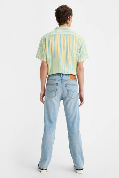 Jean droit bleu clair de Levi's, avec poches arrières, porté avec une chemise rayée jaune et turquoise.