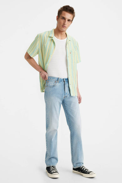 Jean droit en denim bleu clair de Levi's®, porté avec un t-shirt blanc et une chemise rayée ouverte.