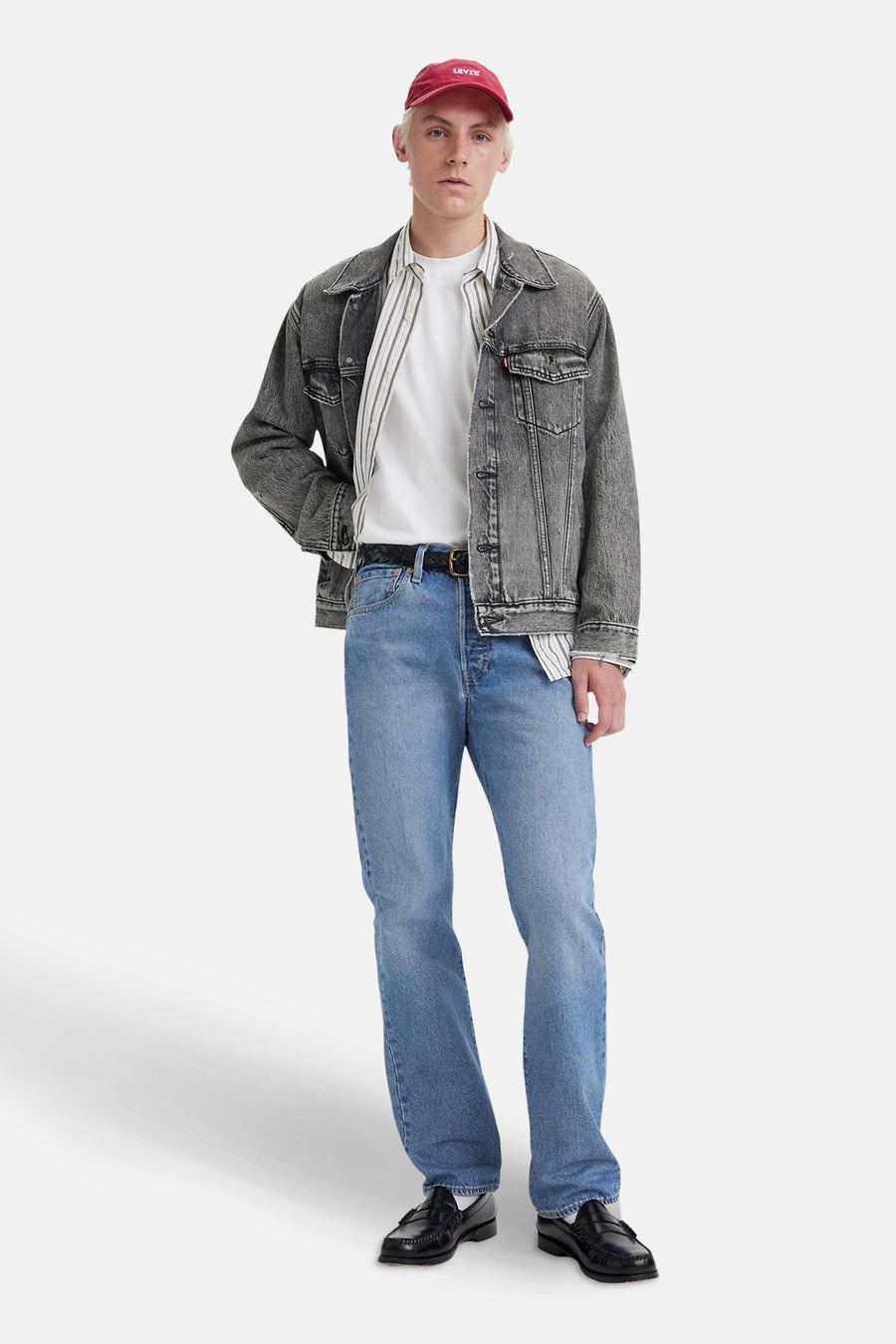 Lichtblauwe rechte jeans van Levi's, gedragen met een grijze spijkerjas, een gestreept overhemd en een rode pet.