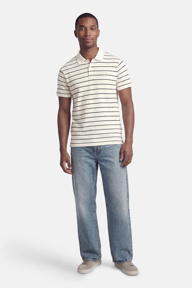 Wit poloshirt met zwarte strepen van Levi's®, gedragen met een blauwe spijkerbroek en grijze sneakers.