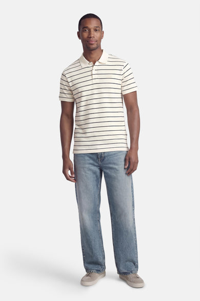 Wit poloshirt met zwarte strepen van Levi's®, gedragen met een blauwe spijkerbroek en grijze sneakers.