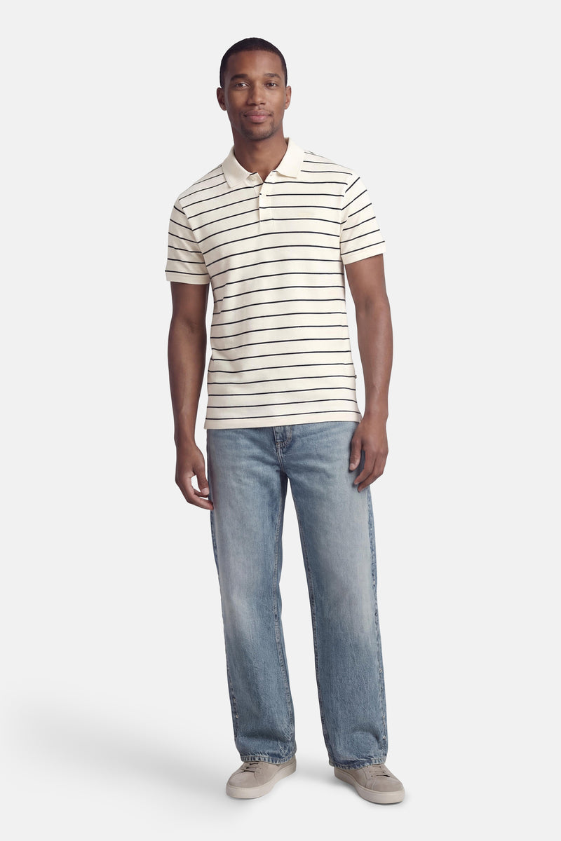 Wit poloshirt met zwarte strepen van Levi's®, gedragen met een blauwe spijkerbroek en grijze sneakers.