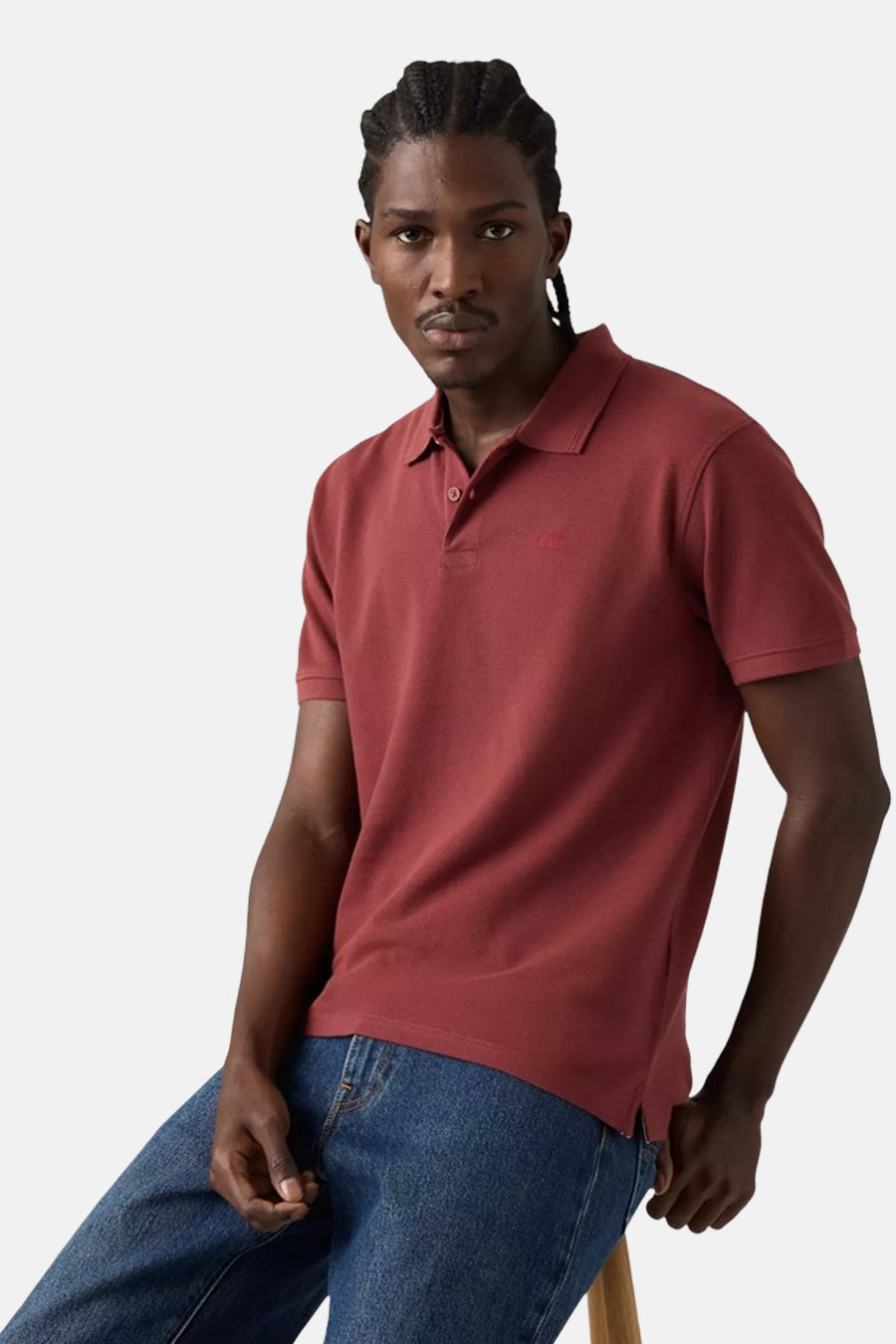 Polo bordeaux à manches courtes de Levi's®, porté avec un jean bleu et tresses visibles.