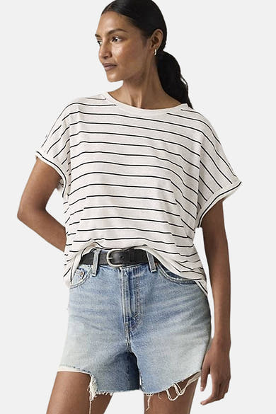 T-shirt à manches courtes blanc à rayures noires par Levi's, porté avec des shorts en jean délavé et une ceinture noire.