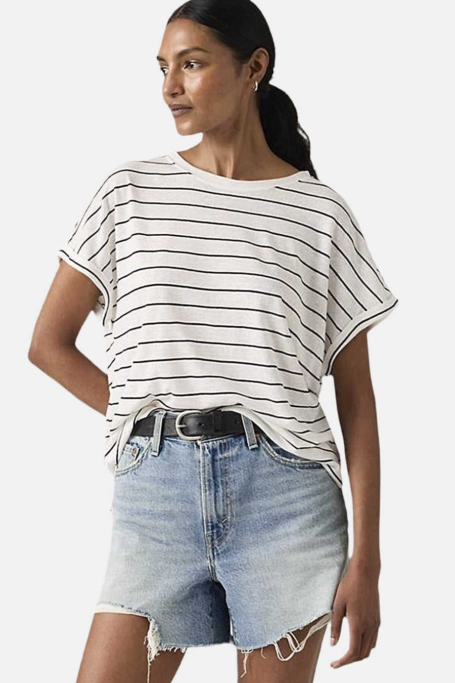 T-shirt à manches courtes blanc à rayures noires par Levi's, porté avec des shorts en jean délavé et une ceinture noire.