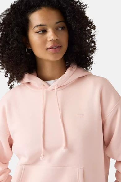 Rose pink oversized hoodie with drawstring hood and front pocket, worn by model with curly hair, side view