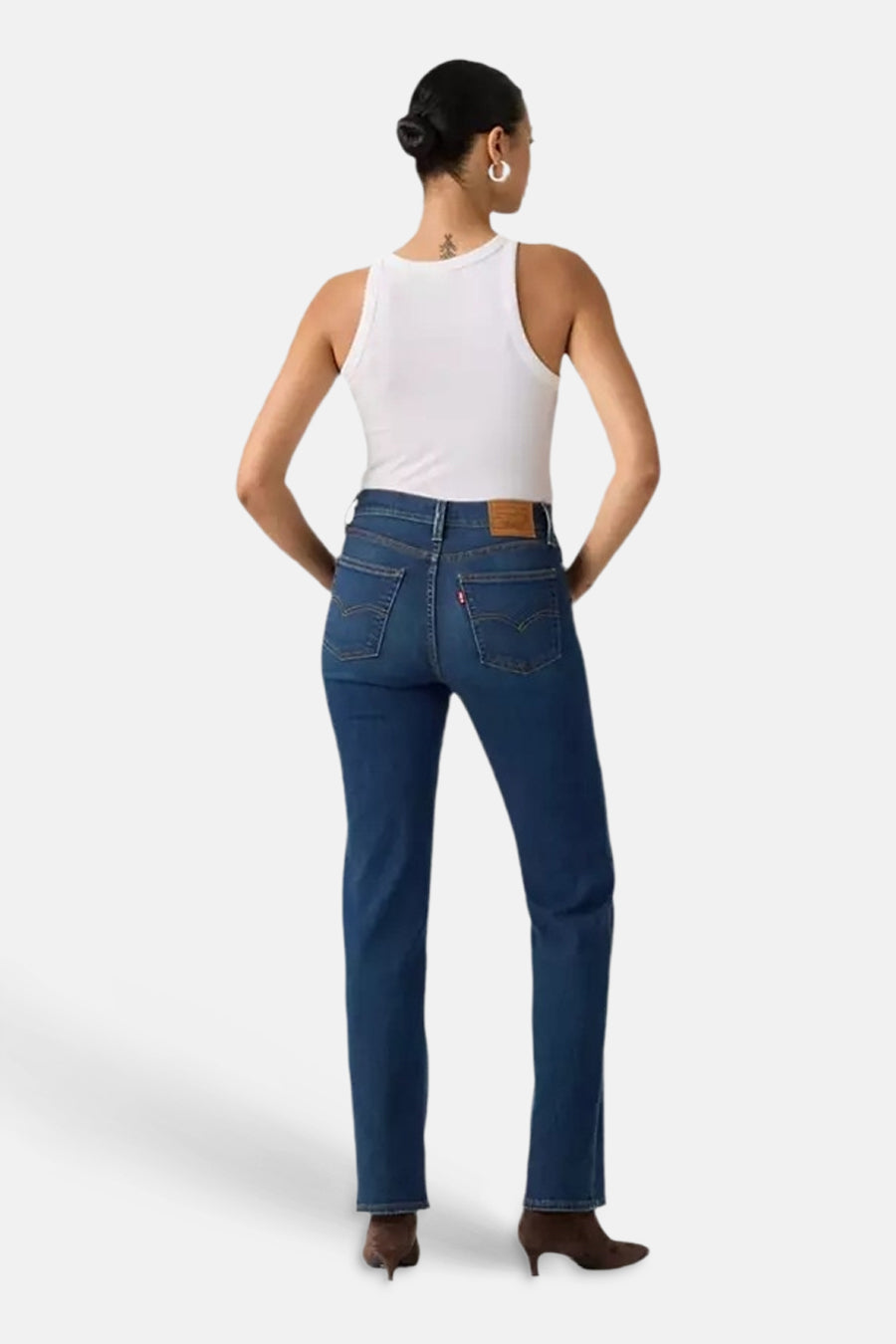 Dark blue straight-leg denim jeans by Levi's, back view with classic stitching and brown leather waistband patch, worn with white tank top and brown heeled boots