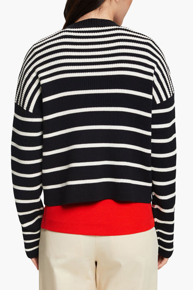Pull ras du cou noir à rayures blanches par Esprit, porté avec un t-shirt rouge et un pantalon beige.