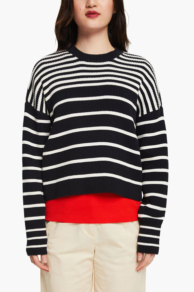 Pull noir à rayures blanches par Esprit, porté avec un t-shirt rouge et un pantalon beige.