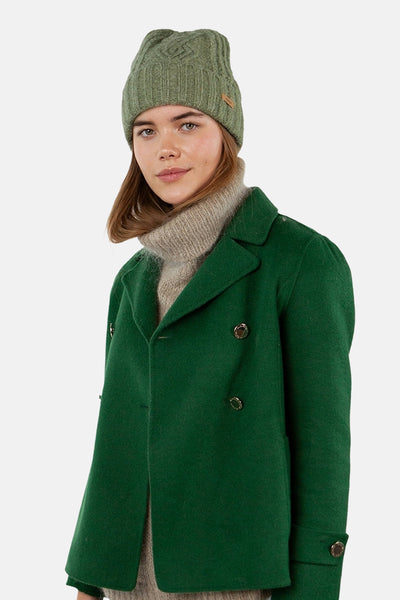 Bonnet vert en maille torsadée de BARTS, porté avec un manteau vert et un pull à col roulé beige.