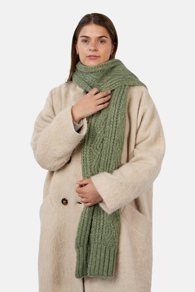 Écharpe verte en tricot torsadé de Barts, portée avec un manteau beige texturé.
