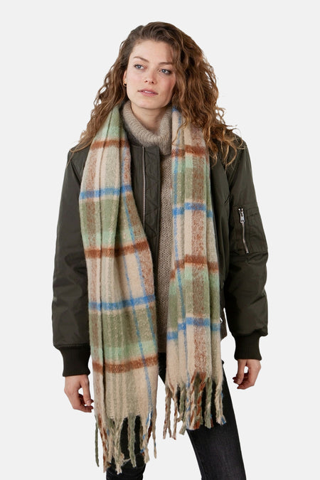 Écharpe à carreaux en laine verte de BARTS, avec des motifs beiges et bleus, portée avec un pull col roulé et une veste.
