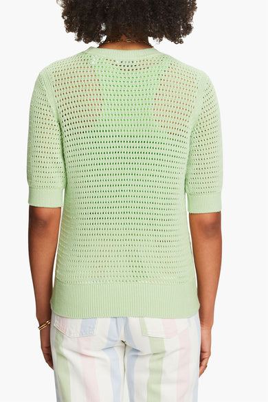 Pull à col rond vert d'Esprit, à mailles ajourées porté sur un débardeur assorti et un pantalon rayé pastel.
