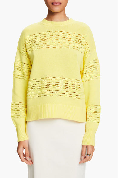 Gele rondehals trui van Esprit, met ajourdetails en gedragen met een witte rok.