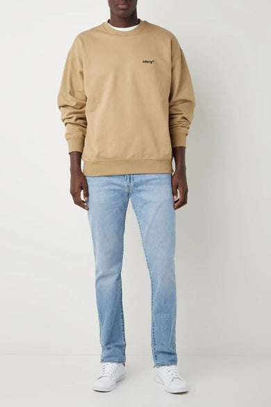 Jean slim en denim bleu clair de Levi's®, porté avec un pull beige et des baskets blanches