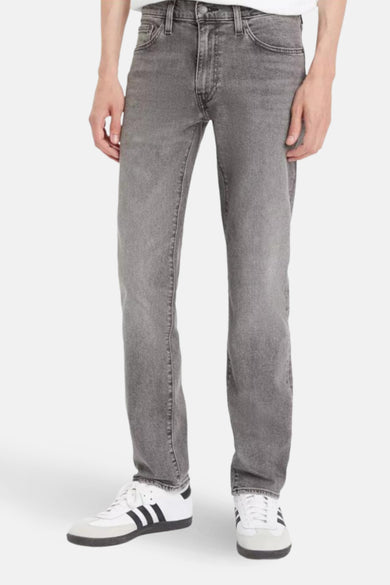 Jean slim gris clair de Levi's, porté avec des baskets blanches à rayures noires.
