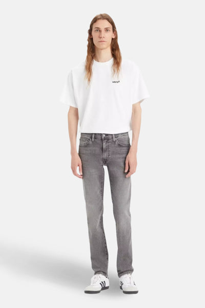 Jean slim gris clair de Levi's, porté avec un t-shirt blanc uni et des chaussures de sport blanches.