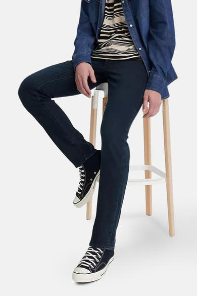 Slim jeans in donkerblauw denim van Levi's, gedragen met een gestreept T-shirt en een groene pet.