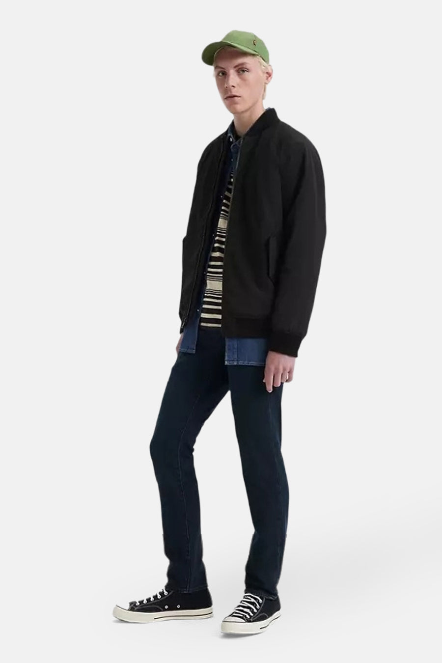 Slim jeans in donkerblauw denim van Levi's®, gedragen met een zwart jasje, een gestreept overhemd en zwarte lage sneakers.