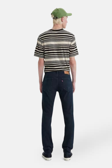 Jean slim en denim bleu foncé de Levi's, porté avec un t-shirt rayé et une casquette verte.