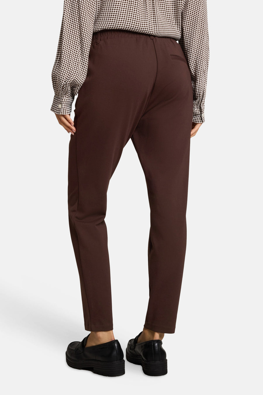 Brown five-pocket women's seasonal trousers with elastic waist, back view, paired with polka-dot blouse and black loafers