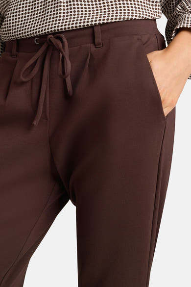 Brown five-pocket women's seasonal pants with drawstring waist and soft knit texture, shown in front view with hand in side pocket