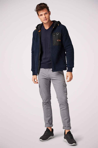 Pull bleu marine à col en V par Tom Tailor, porté avec un gilet à capuche en laine bouclée et un pantalon cargo gris.