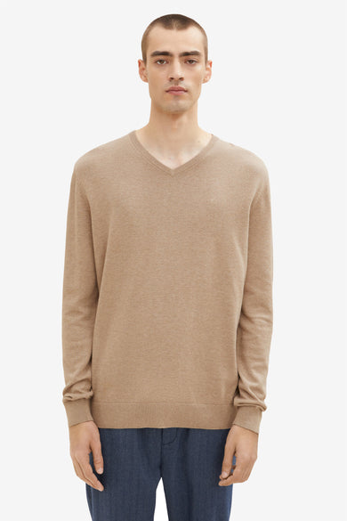 Pull col V beige de Tom Tailor, en maille fine, porté avec un pantalon bleu marine uni.