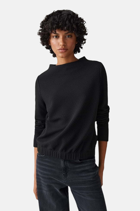 Zwarte rondehals trui van OPUS, getextureerd, gedragen met een wijde jeans en bordeaux loafers.