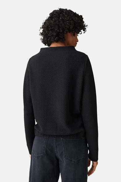 Pull à col rond noir par OPUS, avec une texture gaufrée subtile, porté avec un jean foncé.
