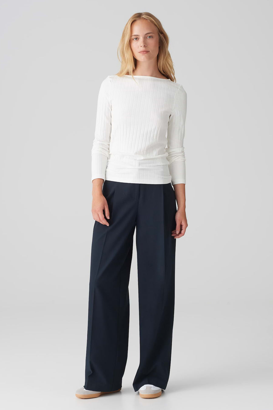 Pull à col rond blanc de OPUS, en maille côtelée, porté avec un pantalon large bleu marine.