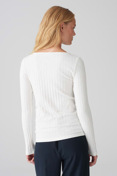 Pull à col rond blanc par OPUS, en maille côtelée, porté avec un pantalon bleu marine.