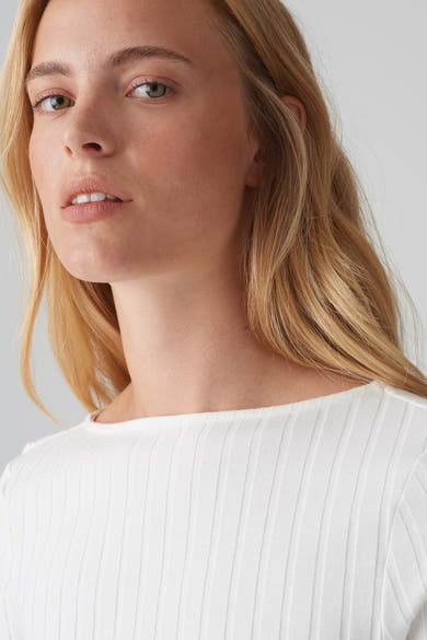 Pull à col rond blanc de OPUS, en maille côtelée fine, porté par un modèle blond au teint clair.

