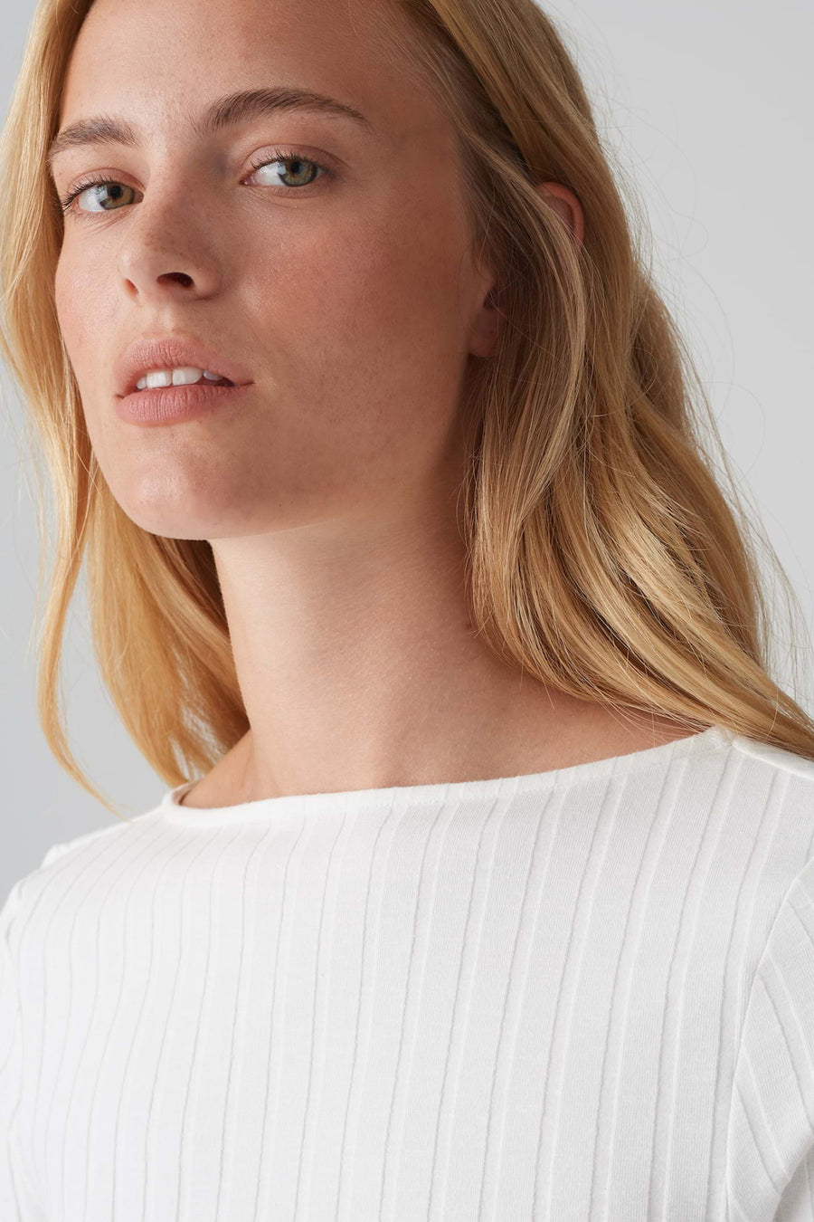Pull à col rond blanc de OPUS, en maille côtelée fine, porté par un modèle blond au teint clair.
