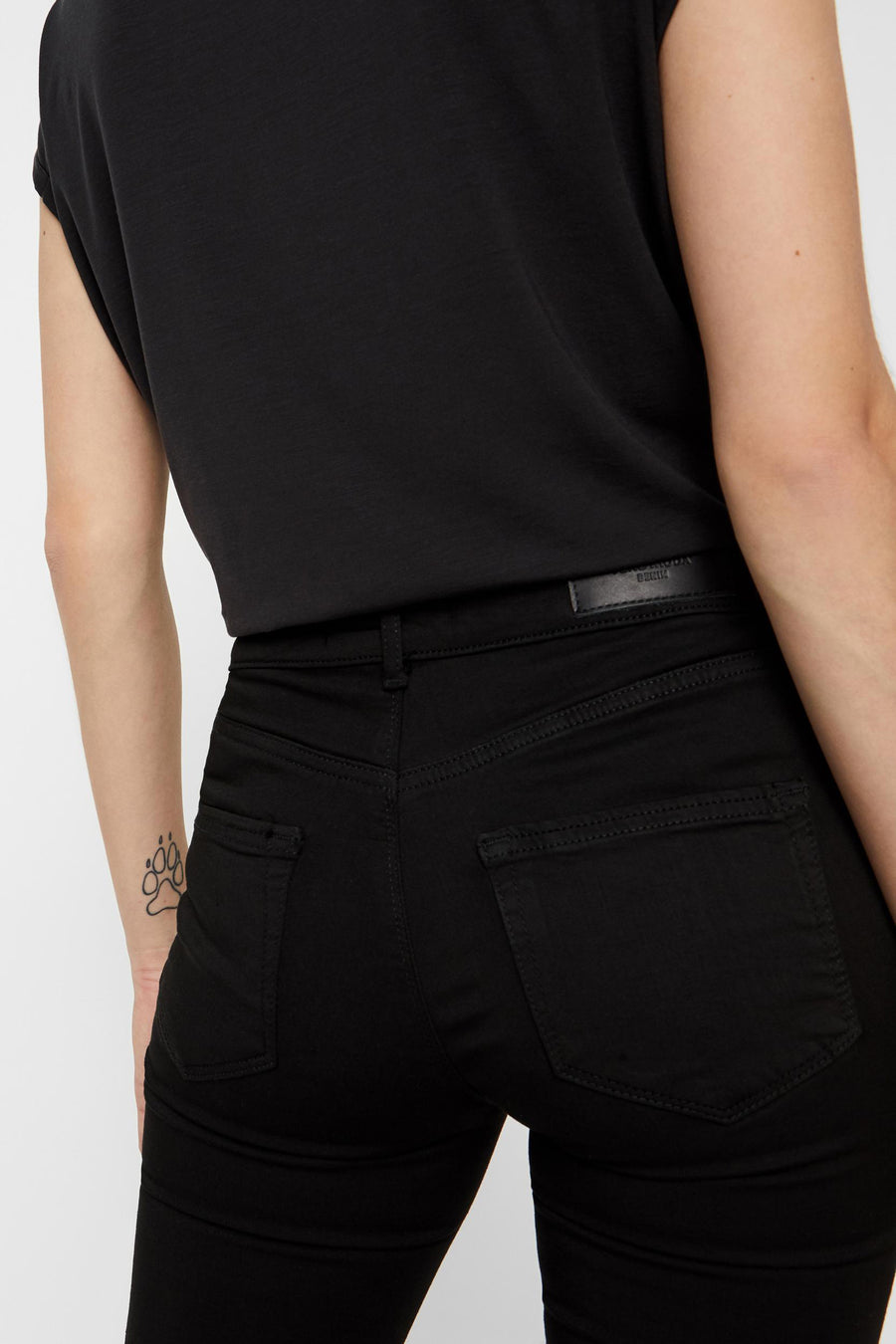 Jean skinny noir de VERO MODA, coupe taille haute, avec poches arrière et un tatouage sur le poignet.
