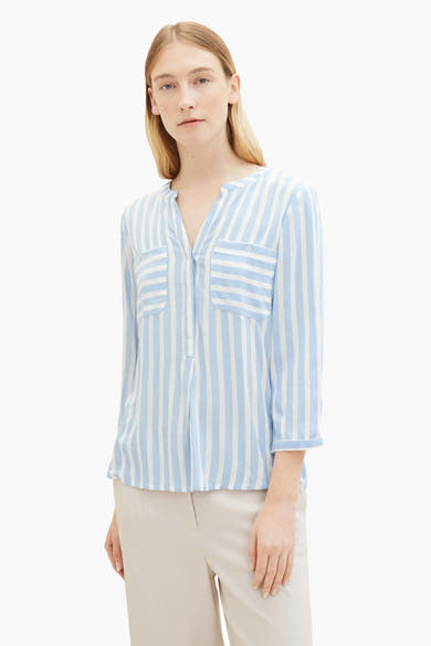 Blouse à manches longues bleue rayée de Tom Tailor, avec poches poitrine et pantalon beige porté.
