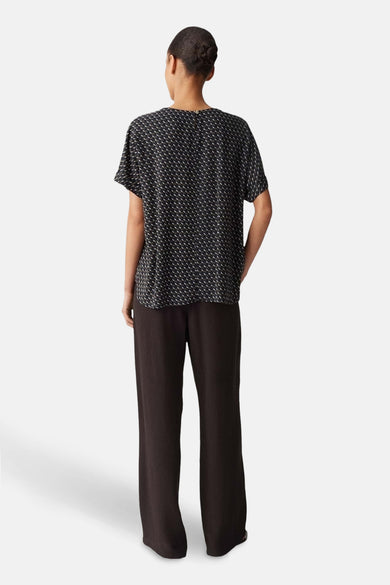 Blouse multicolore à manches courtes par OPUS, avec un motif géométrique discret, portée avec un pantalon marron.
