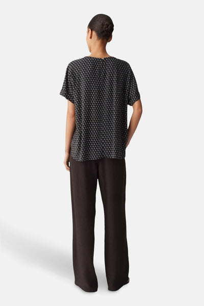 Blouse multicolore à manches courtes par OPUS, avec un motif géométrique discret, portée avec un pantalon marron.
