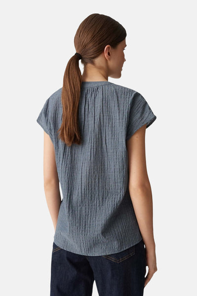 Blouse à manches courtes bleue OPUS, à texture froissée, portée avec un jean bleu foncé, vue de dos.