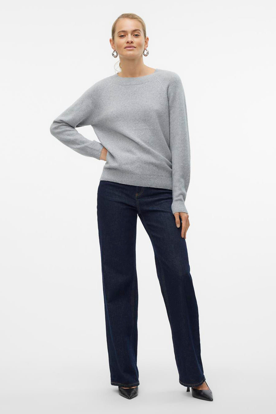 Pull col rond gris de VERO MODA, porté avec un jean bleu marine et des escarpins noirs.