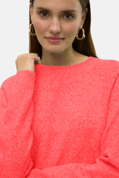 Pull à col rond orange par Vero Moda, en maille douce, porté par une femme avec des boucles d'oreilles dorées.