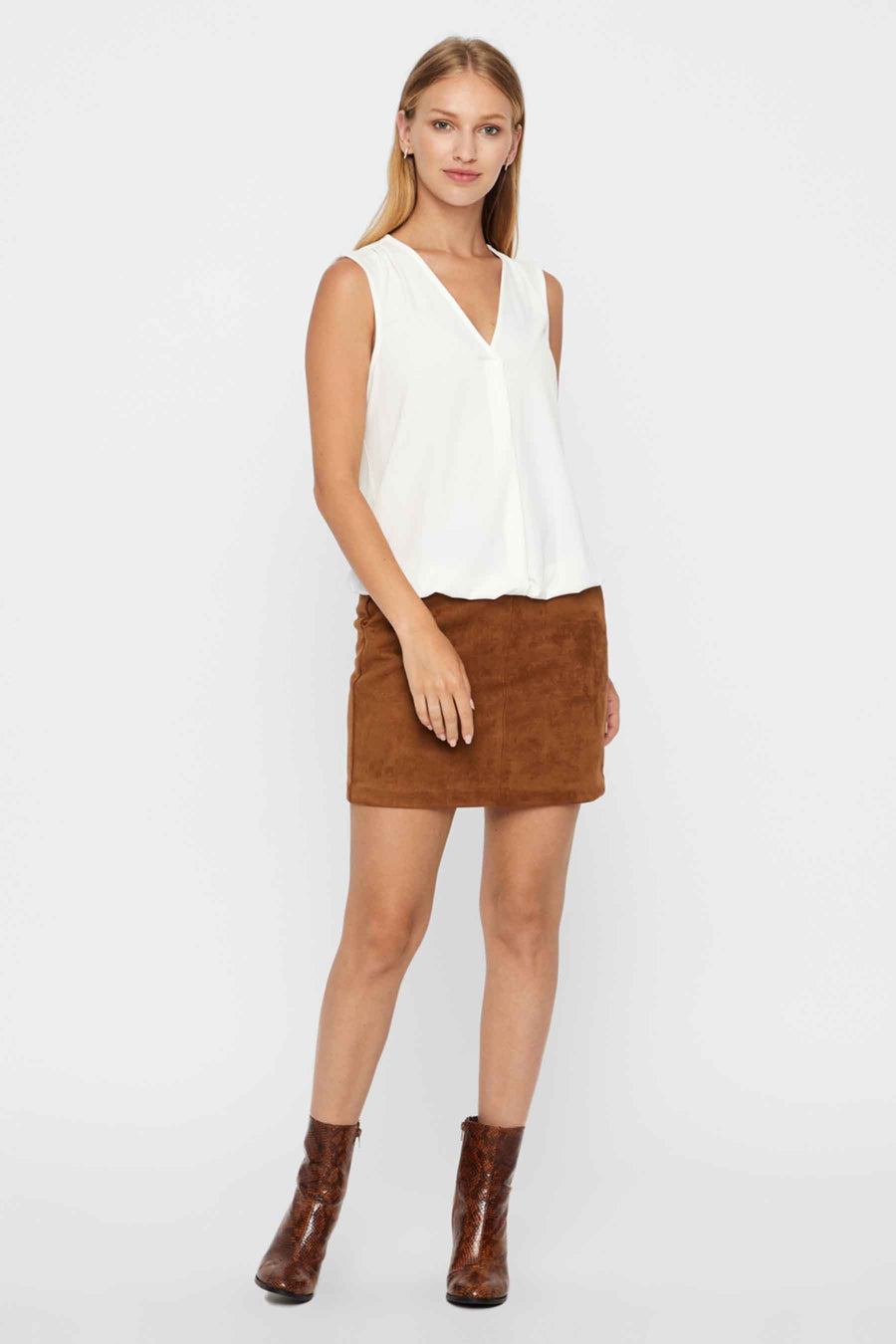 Mini-jupe marron en suède de Vero Moda, portée avec un haut blanc sans manches et des bottines à motif peau de serpent.